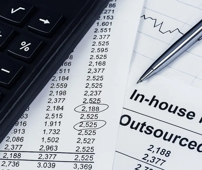 A calculator, pen, and papers with financial data and lists comparing in-house and outsourced costs.