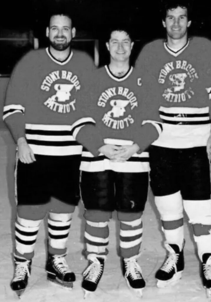 Three hockey players in "Stony Brook Patriots" jerseys stand side by side on an ice rink, posing for a group photo.