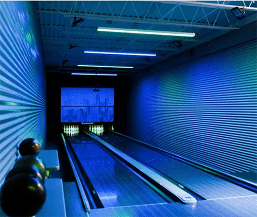 A modern bowling alley with two lanes, three bowling balls on a rack, and blue lighting illuminating the space—showcasing how about flexible IT can transform leisure environments.