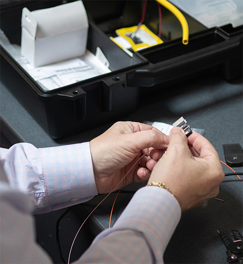 A person in a dress shirt holds fiber optic cables while working at a desk with electronic components and an open black tool case, showcasing the importance of flexible IT solutions.